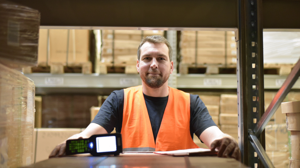 Warehouse operative in an orange hi-vis vest holding a handheld scanner