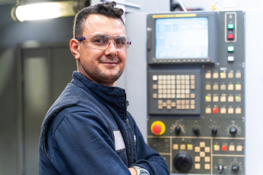 CNC machinist smiling beside a CNC machine control panel