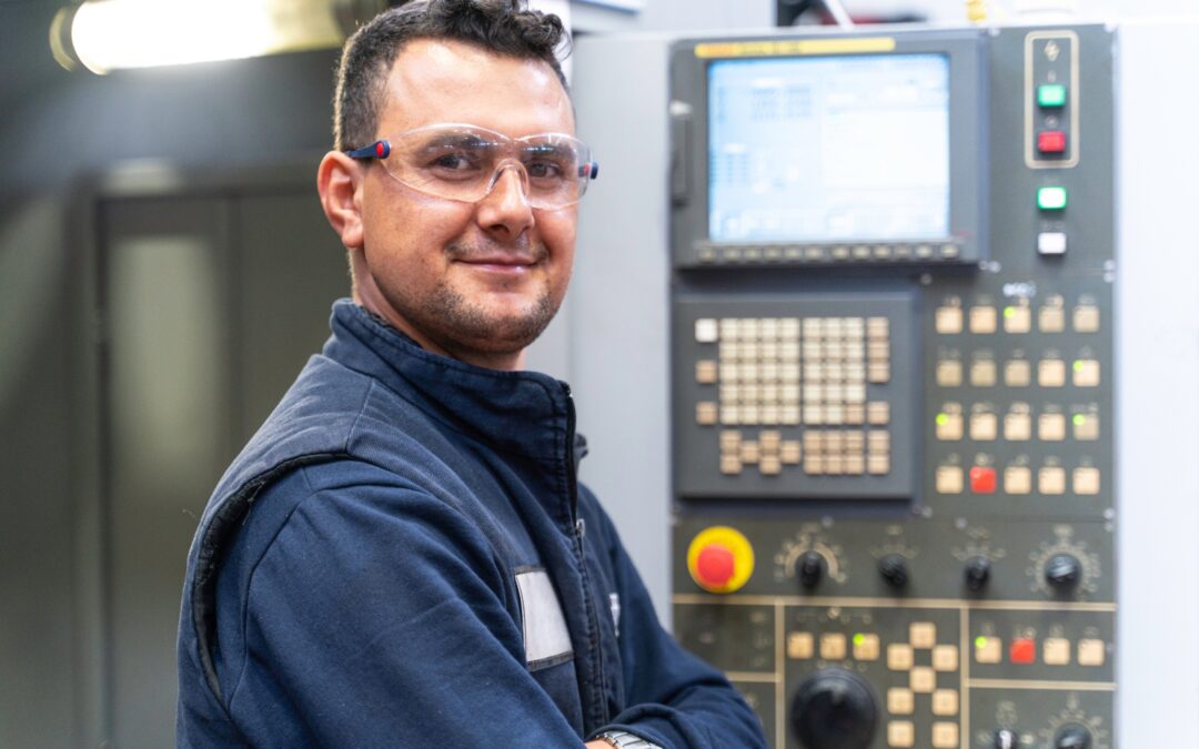 CNC machinist smiling beside a CNC machine control panel