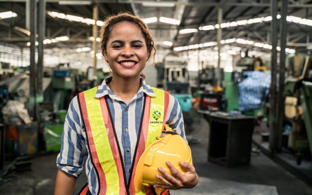 Smiling industrial worker in a hi-vis vest holding a hard hat on a factory floor